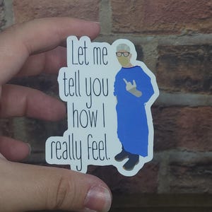 May include: White sticker with a cartoon illustration of a person wearing a blue surgical gown and a face mask. The text on the sticker reads "Let me tell you how I really feel."