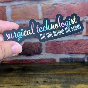 May include: A black sticker with the text "surgical technologist the one behind the mayo" in rainbow colors.