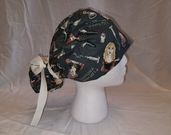 May include: A black scrub hat with a white ribbon tie. The hat features a colorful print of characters from the movie Hocus Pocus. The text on the hat reads "It's just a touch of Hocus Pocus".