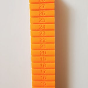 May include: An orange plastic ruler with numbers 12 through 30 printed on it.