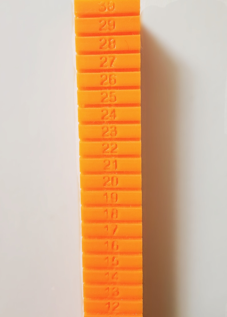 May include: An orange plastic ruler with numbers 12 through 30 printed on it.