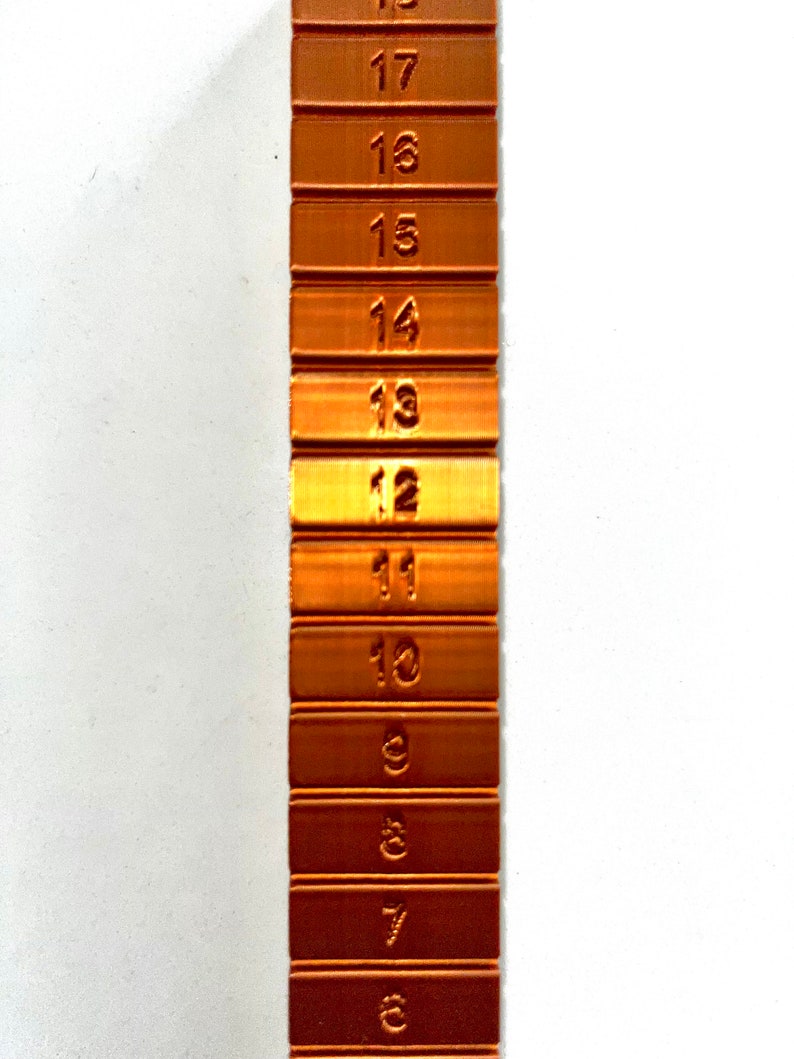 May include: A copper-colored metal ruler with numbers 6 through 18 marked on each section. The ruler is a vertical strip with each number on a separate section.