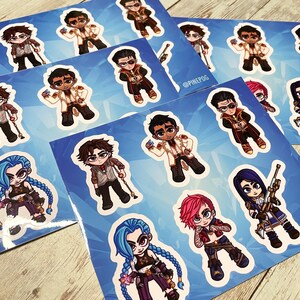 May include: A set of 10 colorful cartoon stickers featuring characters from the video game League of Legends. The stickers are printed on glossy paper and have a white border. The characters include Jinx, Vi, Jhin, and others. The stickers are perfect for decorating laptops, water bottles, and other personal items.