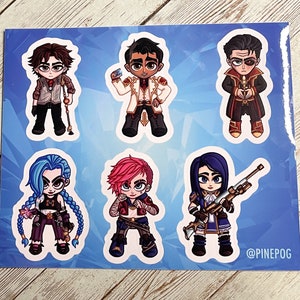 May include: A set of six colorful cartoon character stickers featuring characters from the video game League of Legends. The stickers are printed on white paper with a blue background. The characters include Jinx, Vi, Jayce, Caitlyn, Viktor, and Ekko. The text "@PINEPOG" is printed in the bottom right corner.