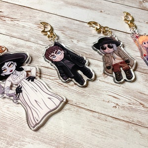 Puede incluir: Cuatro llaveros de acr&iacute;lico coloridos con personajes de dibujos animados. Cada llavero tiene una cadena dorada y un fondo de acr&iacute;lico transparente. Los personajes son una mujer con un vestido blanco y un sombrero negro, un hombre con una chaqueta negra, un hombre con un abrigo marr&oacute;n y gafas de sol, y un hombre con una chaqueta azul.