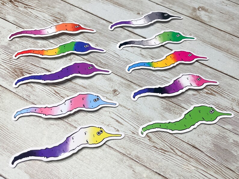 May include: A selection of worm stickers, each displaying a different pride flag design. The stickers feature worms with white borders and a variety of colours, including rainbow, pink, blue, and green.