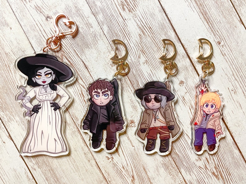 Puede incluir: Cuatro llaveros de personajes de dibujos animados coloridos con cierres de metal dorado. Los personajes son una mujer con un vestido blanco y un sombrero negro, un hombre con un abrigo negro, un hombre con un abrigo marr&oacute;n y gafas de sol, y un hombre con una chaqueta blanca y pantalones vaqueros azules.