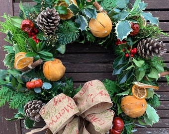 May include: A festive Christmas wreath with a burlap bow that reads "Merry Christmas" in red and green. The wreath is adorned with pinecones, dried orange slices, red berries, and various green foliage, creating a natural and seasonal decoration.