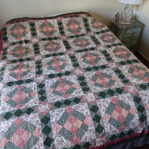 May include: A green, pink and white patchwork quilt with a diamond pattern. The quilt is made of cotton fabric and has a red and green border.