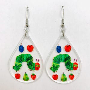 May include: Clear acrylic teardrop earrings featuring a green caterpillar with a red face and a variety of colorful fruits. The earrings have silver-colored fish hook ear wires. The design is inspired by a children's book.