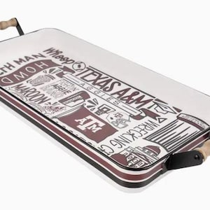May include: Rectangular serving tray with a white surface and maroon and black trim. The tray features the text "Texas A&M" and other related graphics. It has wooden handles on each end.