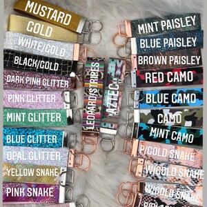 May include: A collection of keychains with various patterns and colors, including mustard gold, white/gold, black/gold, dark pink glitter, pink glitter, mint glitter, blue glitter, opal glitter, yellow snake, pink snake, pale pink snake, leopard/stripes, Aztec, mint paisley, blue paisley, brown paisley, red camo, blue camo, camo, and mint camo.