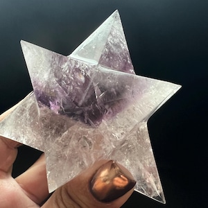 May include: A clear, faceted, purple amethyst star crystal. The star is made of multiple points that come together to form a star shape.