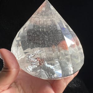 Peut inclure: Un cristal clair et facetté en forme de goutte d'eau. Le cristal est tenu dans une main, avec un fond sombre. Le cristal possède de nombreuses facettes qui réfléchissent la lumière, créant un effet scintillant. Le cristal semble être du quartz.