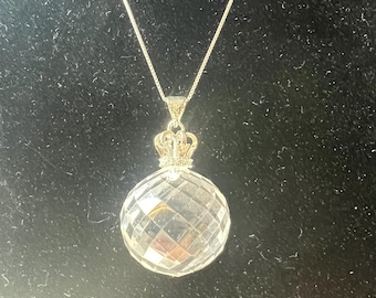 May include: A silver chain necklace with a clear crystal pendant and a gold crown on top.