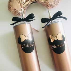 Puede incluir: Dos vasos de color oro rosa con pajitas negras y lazos negros. Los vasos tienen un dise&ntilde;o de Minnie Mouse en blanco y negro con los nombres "Caitlynn" y "Chandler" impresos en ellos. Los vasos est&aacute;n sobre una superficie blanca.