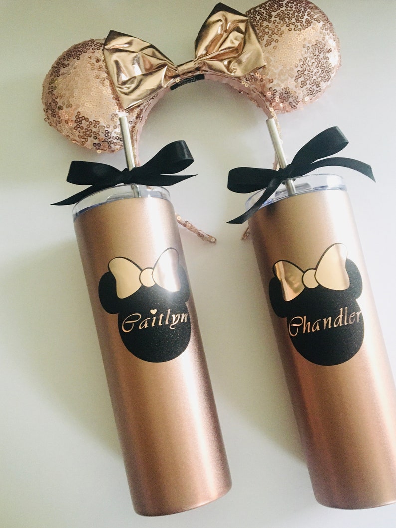 Puede incluir: Dos vasos de color oro rosa con pajitas negras y lazos negros. Los vasos tienen un dise&ntilde;o de Minnie Mouse en blanco y negro con los nombres "Caitlynn" y "Chandler" impresos en ellos. Los vasos est&aacute;n sobre una superficie blanca.