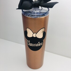 Puede incluir: Un vaso de acero inoxidable color oro rosa con un lazo negro, un dise&ntilde;o de Minnie Mouse en blanco y negro y el nombre "Chamaine" en letras doradas.