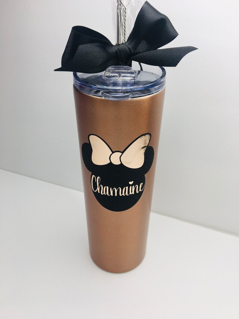 Puede incluir: Un vaso de acero inoxidable color oro rosa con un lazo negro, un dise&ntilde;o de Minnie Mouse en blanco y negro y el nombre "Chamaine" en letras doradas.
