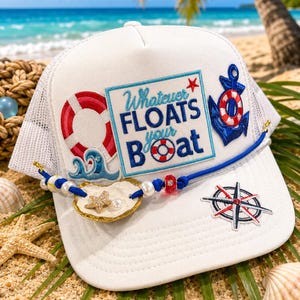 May include: A white trucker hat featuring a rectangular patch with the text Whatever FLOATS your Boat, a red and white life preserver, a blue anchor, a compass rose, and a blue cord adorned with white pearls and a gold-toned seashell.