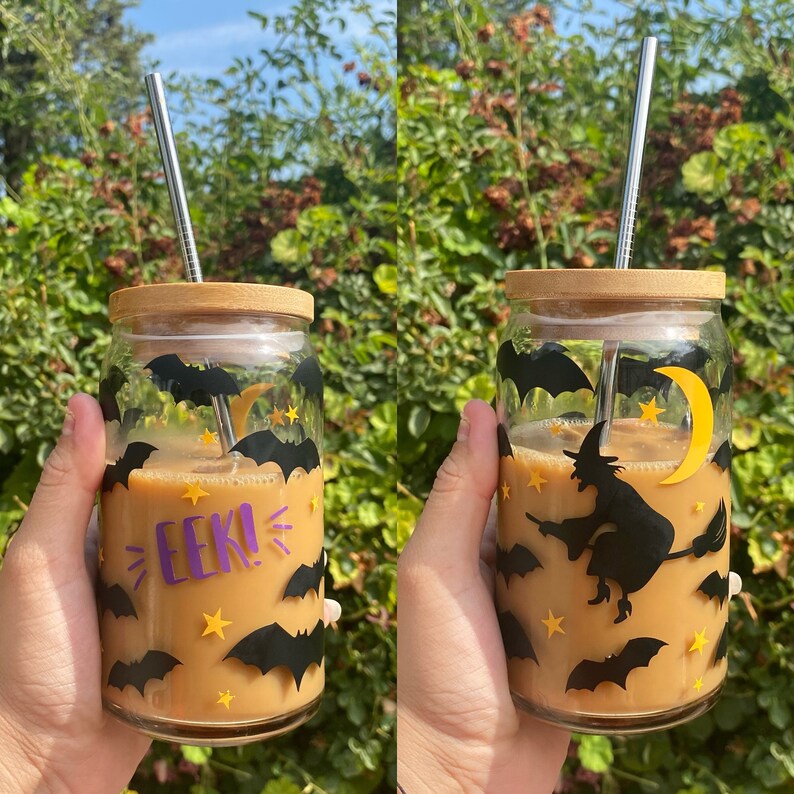 May include: A clear glass jar with a bamboo lid and a metal straw, filled with a light brown beverage. The jar is decorated with black bats, yellow stars, and the word "EEK!" in purple. A witch on a broom flies past a yellow crescent moon.