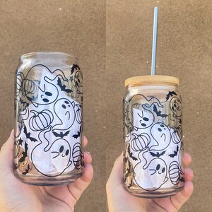 以下が含まれることがあります： ハロウィーンをテーマにしたデザインの、透明なガラス製の缶型タンブラー。デザインは、幽霊、カボチャ、コウモリの黒いイラストが特徴です。1つのタンブラーには竹製の蓋と銀色のストローが付いています。