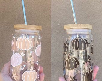 May include: Two glass tumblers with bamboo lids and metal straws. Both tumblers feature a pattern of pumpkins, stars, and flowers. One tumbler has a pink and white pumpkin pattern, while the other has a black and white pumpkin pattern.