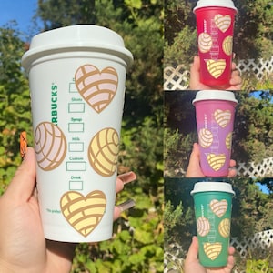 Könnte beinhalten: Drei wiederverwendbare Starbucks-Becher mit weißem Hintergrund und einem Design aus rosa und gelben herzförmigen Gebäck. Die Becher sind rot, rosa und grün.
