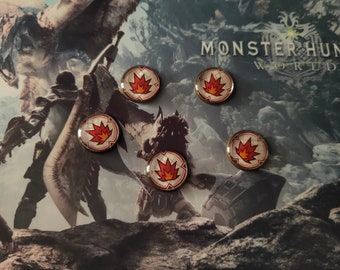 May include: Five round, gold-colored pins with a red and orange flame design on a white background. The pins are arranged in a circle on a background image of a video game character and the text "Monster Hunter World".