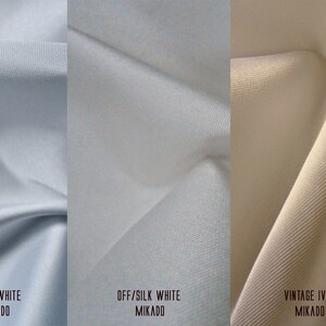 K&ouml;nnte beinhalten: Drei Stoffmuster in verschiedenen Wei&szlig;t&ouml;nen: Reinwei&szlig;, Off-White und Vintage Ivory. Jedes Muster ist mit der Farbe und dem Stofftyp Mikado beschriftet.