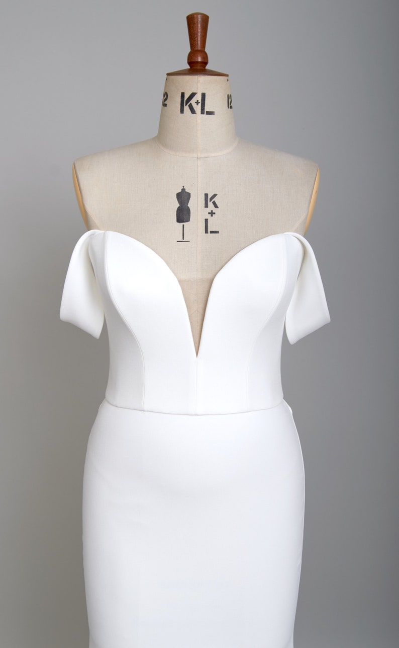 K&ouml;nnte beinhalten: Ein wei&szlig;es, schulterfreies Brautkleid mit tiefem Ausschnitt und einer figurbetonten Silhouette.