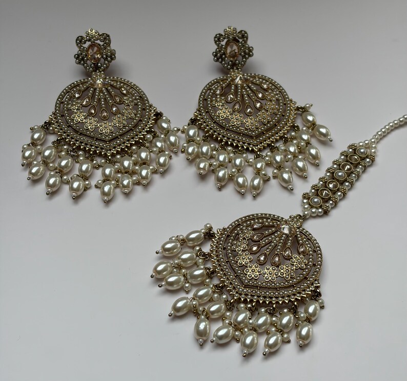 May include: A set of antique gold-toned earrings and a headpiece. The earrings and headpiece feature intricate filigree designs, small clear stones, and dangling faux pearls. The jewelry is likely for a special occasion.