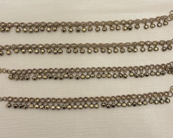 May include: Four silver-toned anklets with small, dangling bells. Each anklet features a chain with alternating circular and bell-shaped charms. The anklets are displayed on a light-colored, textured surface.