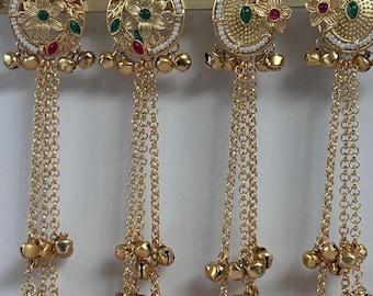 May include: Four gold-colored earrings with intricate floral designs and dangling chains. Each earring features a circular top adorned with red and green gemstones, surrounded by small white beads. The chains end with clusters of small bells.