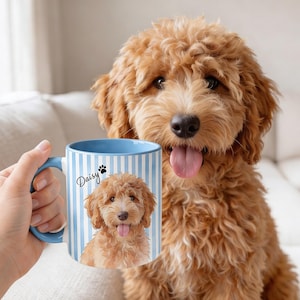 May include: A ceramic mug with a light blue and white vertical striped pattern, featuring a printed image of a golden-brown curly-haired dog and the name Daisy written in black script next to a small black paw print icon.