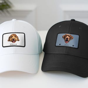 May include: A white baseball cap and a black baseball cap, each featuring a rectangular patch on the front. The white cap displays a golden doodle illustration with the text STELLA. The black cap shows a brown dog illustration with the text Sierra.