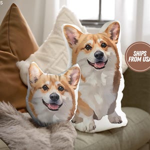 May include: Two white throw pillows with a printed image of a corgi dog. The pillows are on a brown couch with a brown throw blanket.