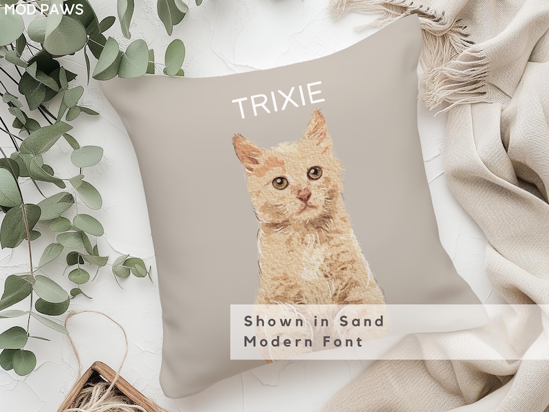 May include: A beige pillow with a light orange cat illustration and the name "TRIXIE" in a white sans-serif font. The text "Shown in Sand Modern Font" is also printed on the pillow.