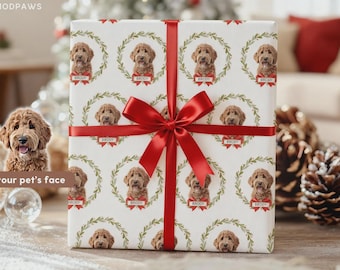 Op de afbeelding: Een vierkante geschenkdoos verpakt in wit papier met een herhalend patroon van een bruine honden kop in een groene krans met een rode strik en de naam Brody eronder gedrukt. Een breed, glanzend rood satijnen lint is in een strik gebonden.