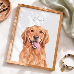 May include: A framed watercolor portrait of a golden retriever dog with its tongue out, featuring the name Charlie written in black script above the dog's head. The artwork is displayed in a light wood frame on a white surface.