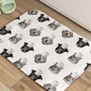 May include: White rectangular bath mat with a repeating pattern of dogs and cats wearing toilet paper hats. The mat is on a wooden floor, with a pair of light green slides visible in the upper left corner. The brand name "MODPAWS" is in the upper left corner.