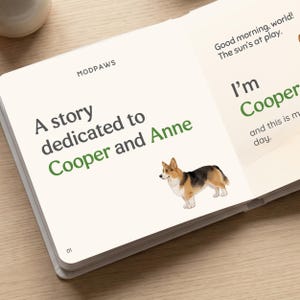 May include: An open book with the text "A story dedicated to Cooper and Anne" and "Good morning, world! The sun's at play." A watercolor illustration of a corgi dog is also present. The book is on a light-colored surface.