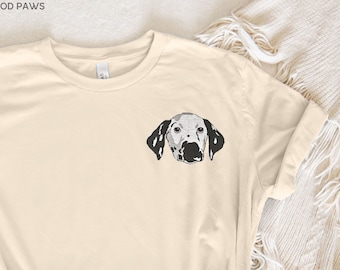 May include: A beige t-shirt with a black and white illustration of a Dalmatian dog's head on the front. The text "MOD PAWS" is visible at the top of the image.