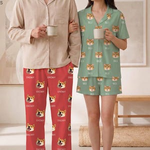 May include: A beige long-sleeved button-down shirt paired with red pajama pants featuring a repeating pattern of a dog face and the text "SNOWY". A sage green short-sleeved button-down pajama top and matching shorts with a repeating cat face and "NALA".