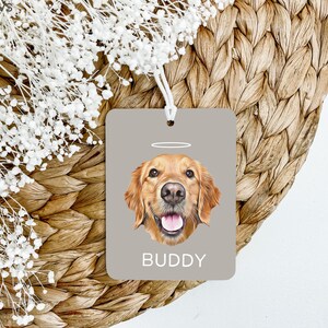May include: A gray car air freshener with a golden retriever dog illustration. The dog has a halo above its head and the text "BUDDY" is printed below the dog.