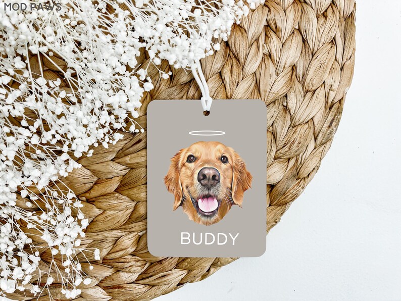 May include: A gray car air freshener with a golden retriever dog illustration. The dog has a halo above its head and the text "BUDDY" is printed below the dog.