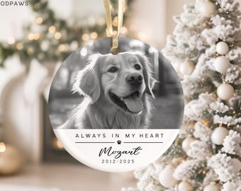 May include: A round, black and white pet memorial ornament with a photo of a Golden Retriever. The ornament has the text "ALWAYS IN MY HEART" and the name "Mozart" with the years 2012-2025. A gold ribbon is attached for hanging.
