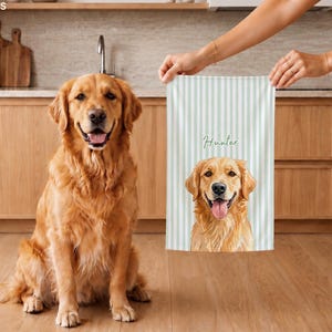 May include: A rectangular kitchen towel featuring a light green and white vertical striped pattern. The towel displays a detailed illustration of a golden retriever with its tongue out, positioned below the name Hunter in cursive script.
