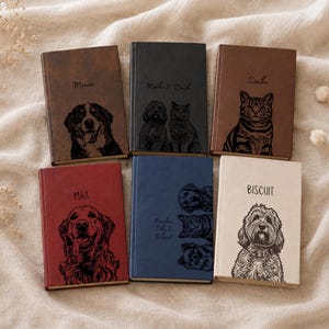 May include: Six rectangular journals in brown, black, tan, red, blue, and cream colours. Each journal features a custom engraved pet portrait and a name. The top left journal says Minnie, top middle says Mochi & Dash, top right says Simba, bottom left says MAX, bottom middle says Frankie, Toby & Biscuit, and bottom right says BISCUIT.
