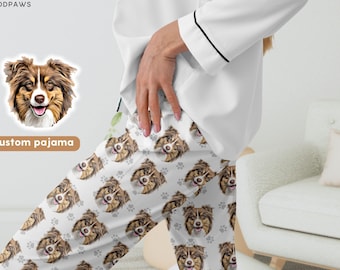 May include: White pajama pants featuring a repeating pattern of brown and white Australian Shepherd dog faces and small gray paw prints. The pants are paired with a plain white long-sleeved pajama top with black trim on the cuffs.